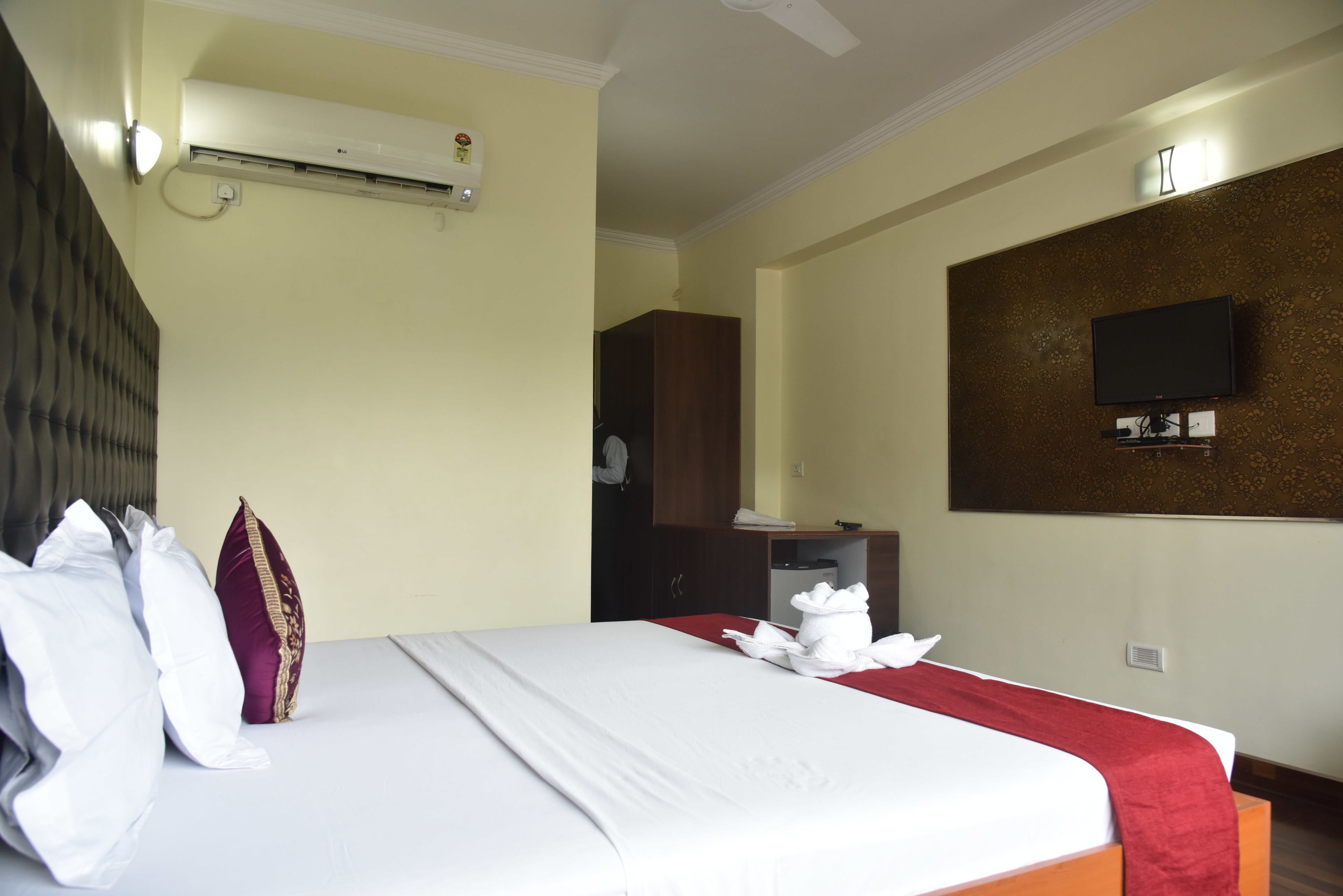 A hotel room with a bed, pillows, a TV, and an air conditioning unit.