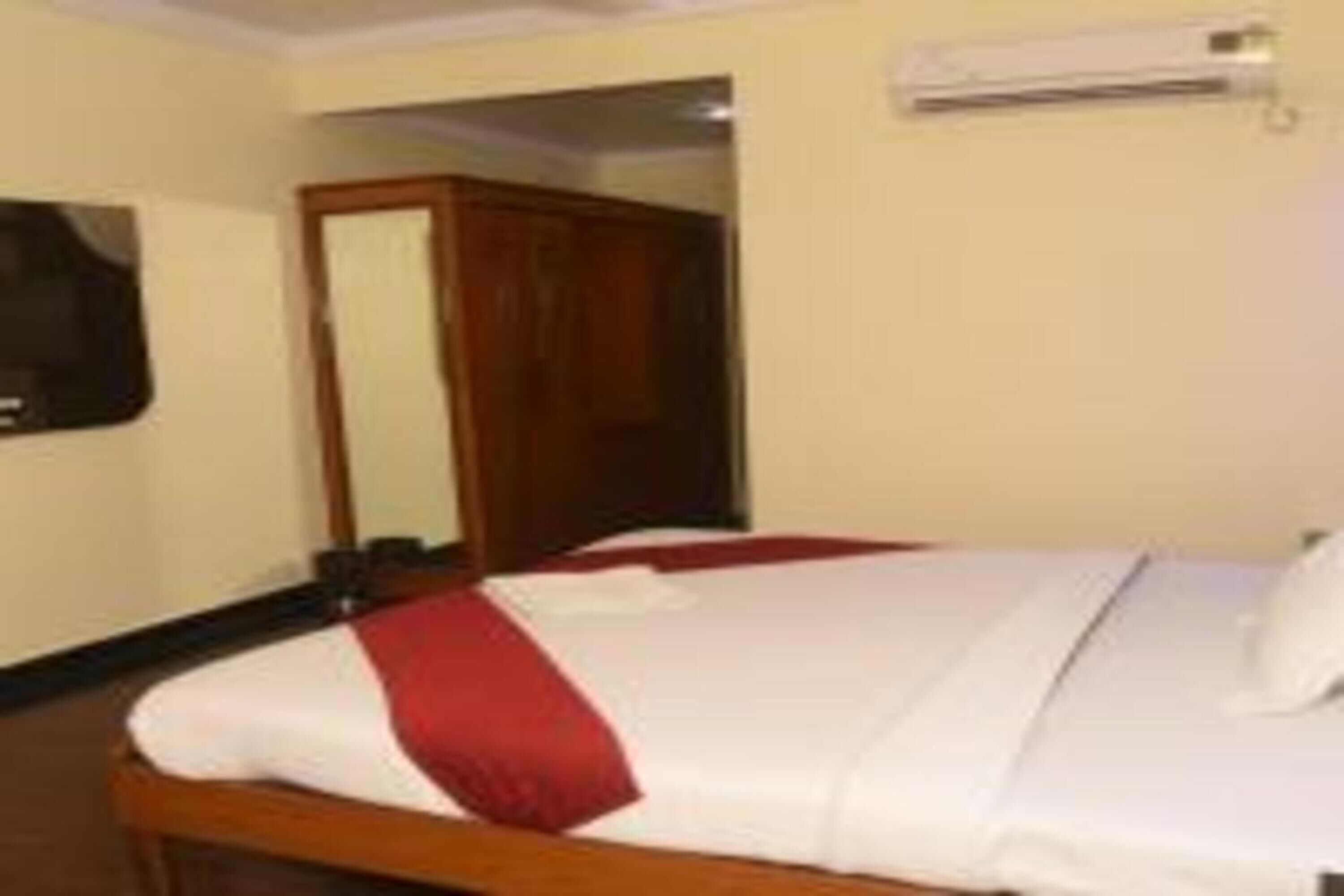 A hotel room with a bed, a wooden headboard, a mirror, and an air conditioning unit on the wall.