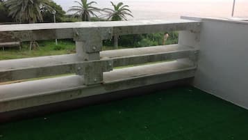 A concrete balcony with steps leading to a green artificial grass floor, overlooking a body of water and palm trees.