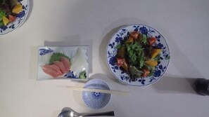 Een tafel met een bord eten, een klein schaaltje met vis en een paar stokjes.