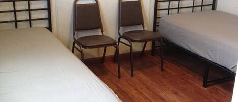 Ein Zimmer mit zwei Einzelbetten, einem Sessel und einem kleinen Schrank.