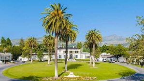 A large, white building with a symmetrical facade, surrounded by a well-maintained lawn and several palm trees.