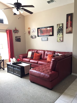 A living room with a red leather sectional sofa, a ceiling fan, and wall decorations including a framed 'Movie Night' sign. - Disney Memories.  4 Bed, 3 Bath, 10 mins from Disney. (Kissimmee)