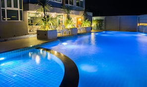 A swimming pool with a curved edge, surrounded by lounge chairs and potted plants.