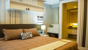 A hotel room with a large bed, a nightstand, a lamp, and a bathroom visible through an open door. - The Near Residence - Sriracha (Si Racha)