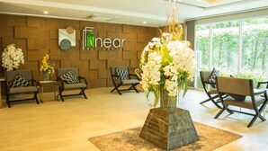 A modern reception area with wooden panel walls, a large window, and a central floral arrangement on a pedestal. - The Near Residence - Sriracha (Si Racha)