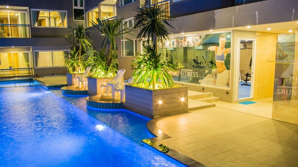 A swimming pool with lounge chairs and palm trees, adjacent to a fitness center. - The Near Residence - Sriracha (Si Racha)
