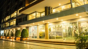 A modern hotel with a glass facade, multiple balconies, and a well-lit entrance. - The Near Residence - Sriracha (Si Racha)