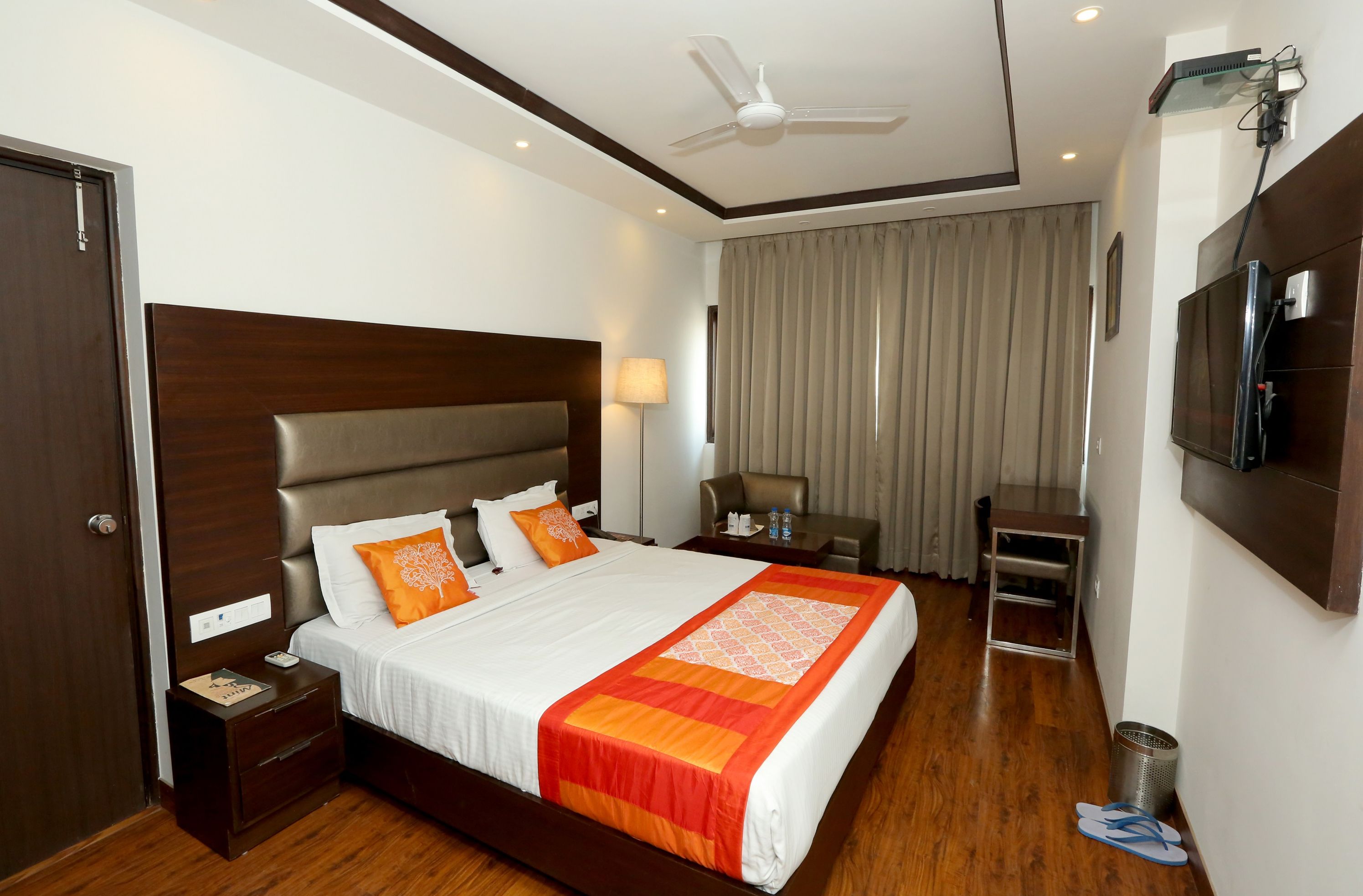 A hotel room with a large bed, a desk, a chair, a TV, and a ceiling fan.