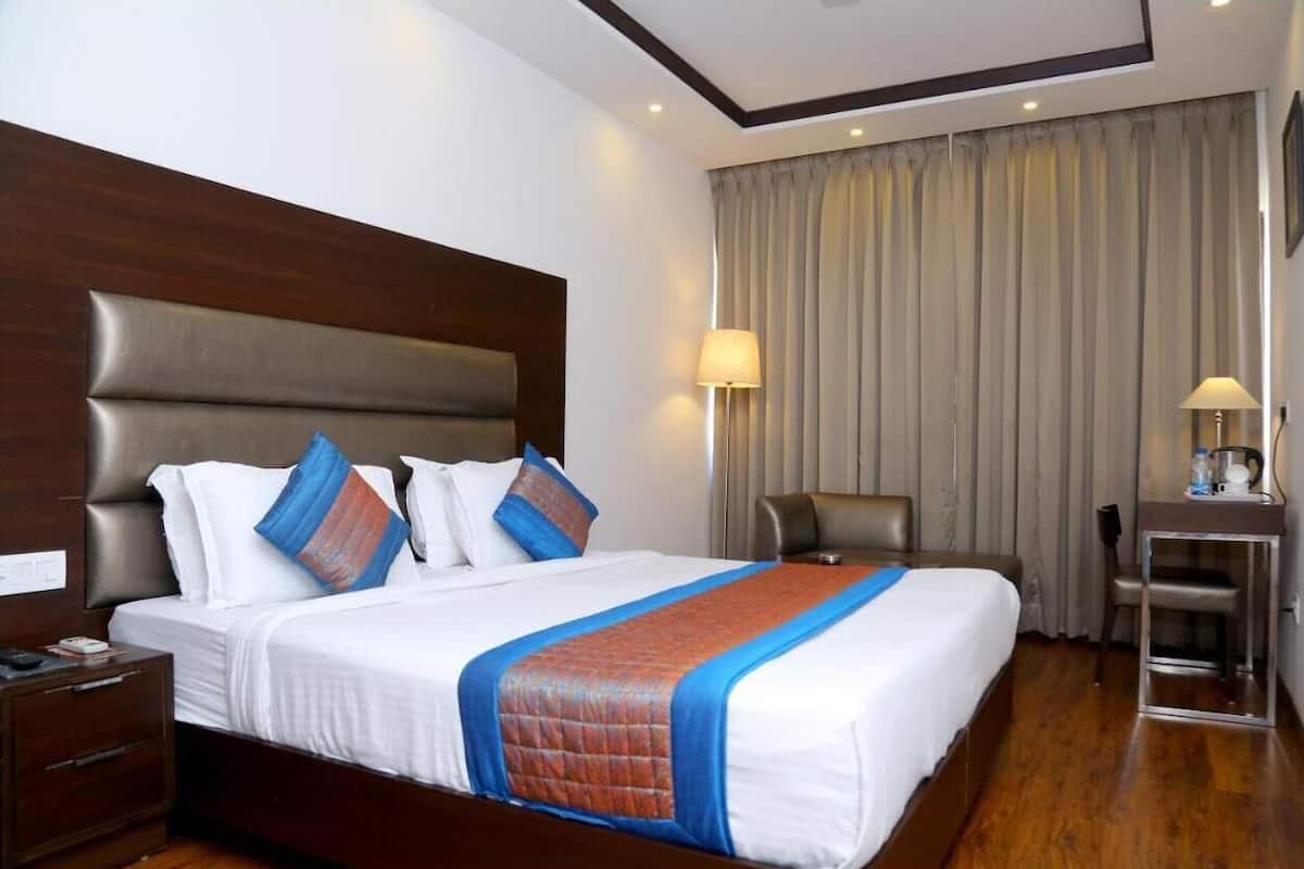 Una habitación de hotel con una cama grande, cabecera de madera, un escritorio con lámpara y una silla.