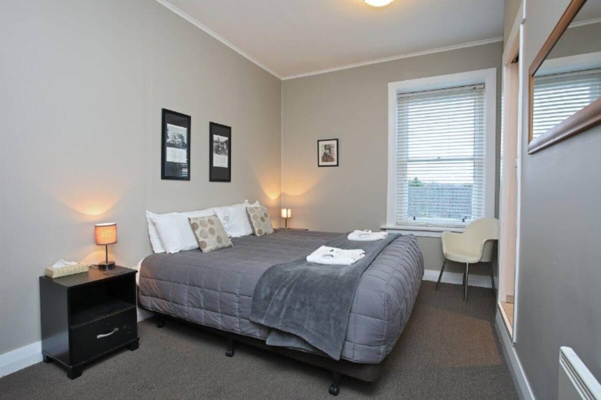 A bedroom with a bed, bedside table, lamp, and a window with blinds.