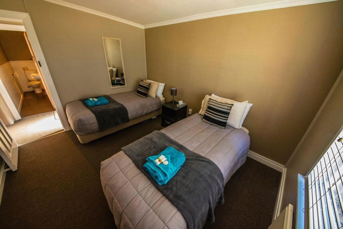 Habitación de hotel con dos camas, un espejo, una mesita de noche y una ventana con barrotes.