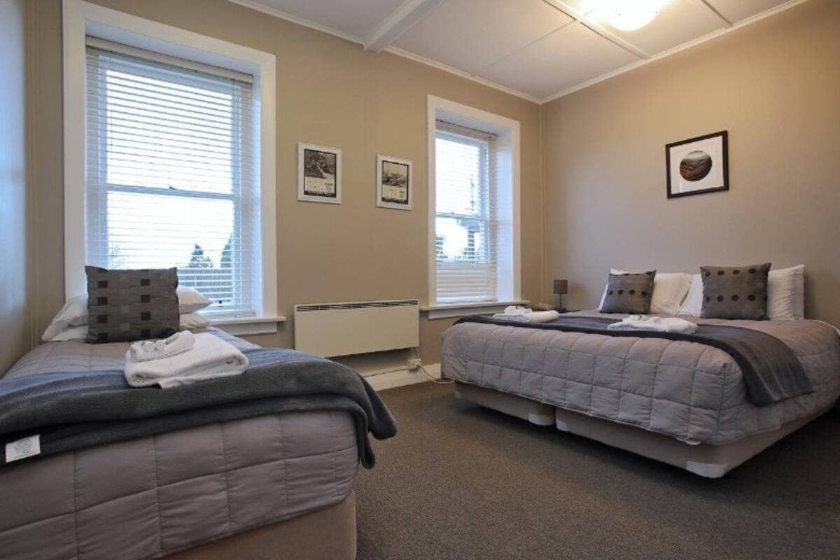 A bedroom with two beds, large windows, and a radiator.