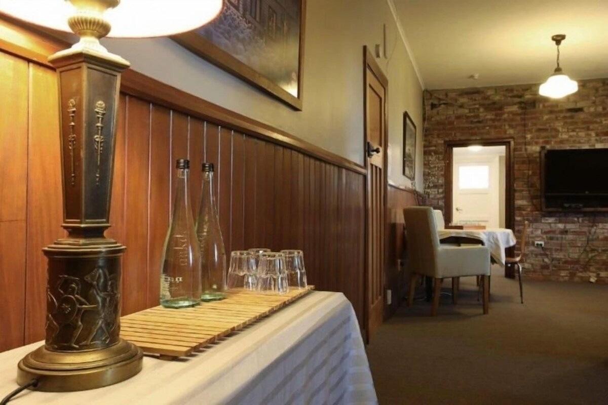 Una habitación con panel de madera, una mesa con lámpara, vasos y botellas, un televisor y una chimenea.