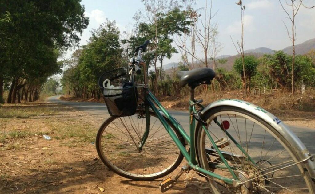 A bicycle parked on a dirt path with a basket attached to the front.