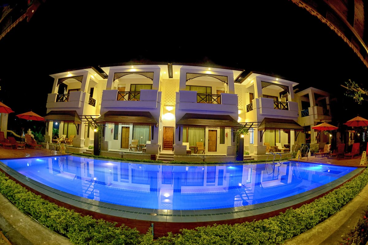 A multi-story hotel with a large swimming pool, outdoor seating, and well-lit balconies.