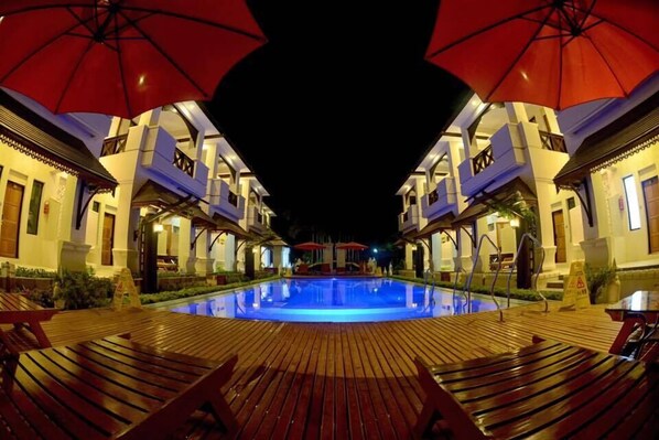 A pool area with wooden deck and red umbrellas, surrounded by buildings with balconies. - Shwe Taung Tan Hotel Lake View (Monywa)