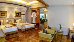 Habitación de hotel con dos camas, una zona de estar con una silla y una mesa, y un armario.