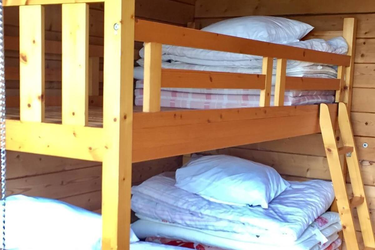Una cama litera con almohadas y mantas, paredes de madera y una escalera.