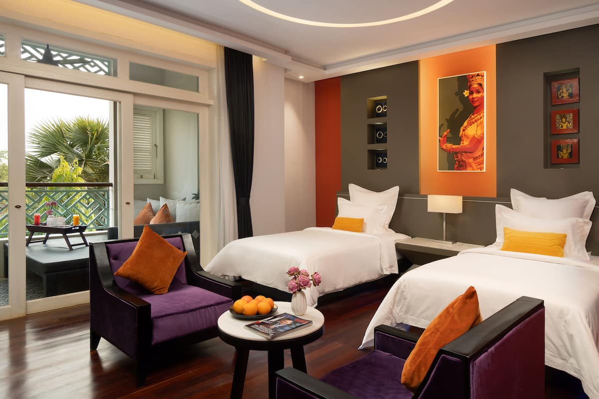 Ein Hotelzimmer mit zwei Betten, einem Balkon mit Tisch und Stühlen sowie Bildern an den Wänden.