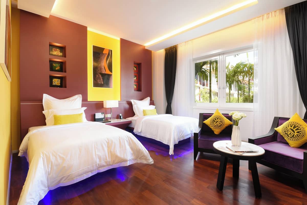 Ein Hotelzimmer mit zwei Betten, einem Sofa, einem kleinen Tisch und einem Fenster mit Vorhängen.