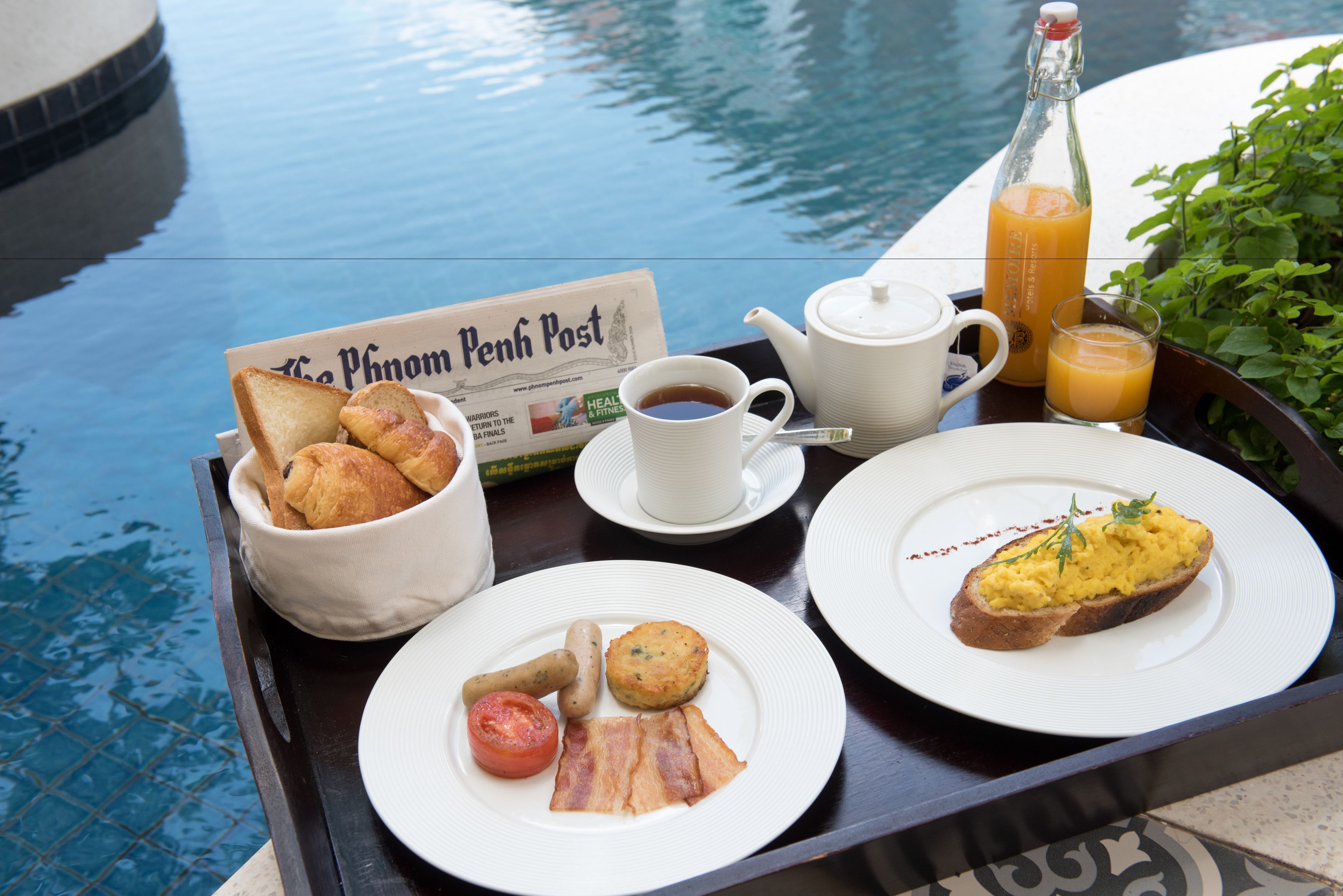 A breakfast tray with toast, eggs, bacon, and a newspaper by a pool.