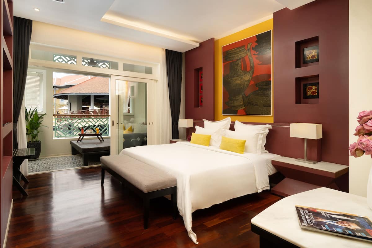 Ein Hotelzimmer mit Bett, Nachttischen, einem Schreibtisch, einer Zimmerpflanze und Blick ins Freie.
