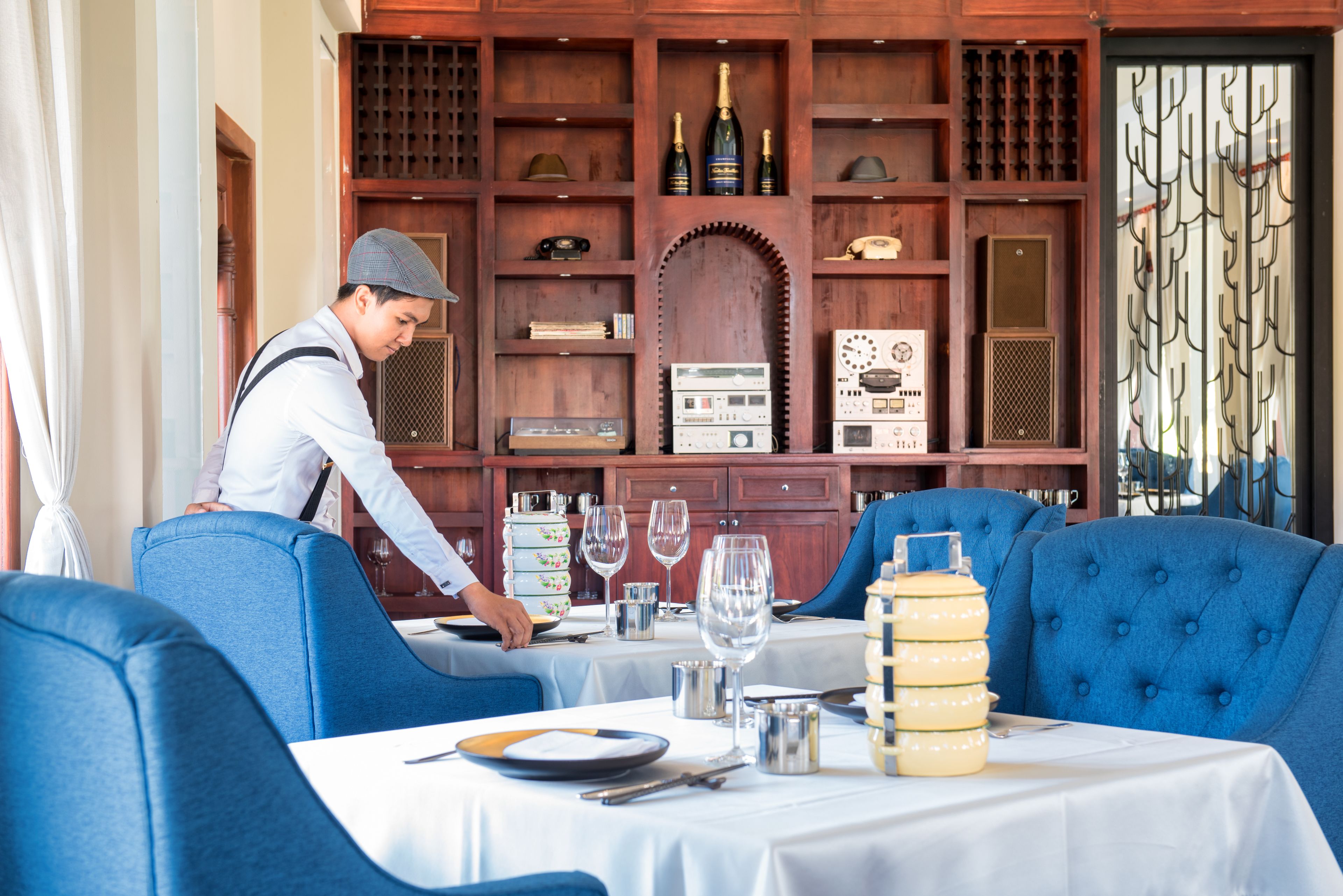 Un restaurant avec des chaises à revêtement bleu, un serveur qui prend les commandes à une table et des radios d’époque exposées sur des étagères.