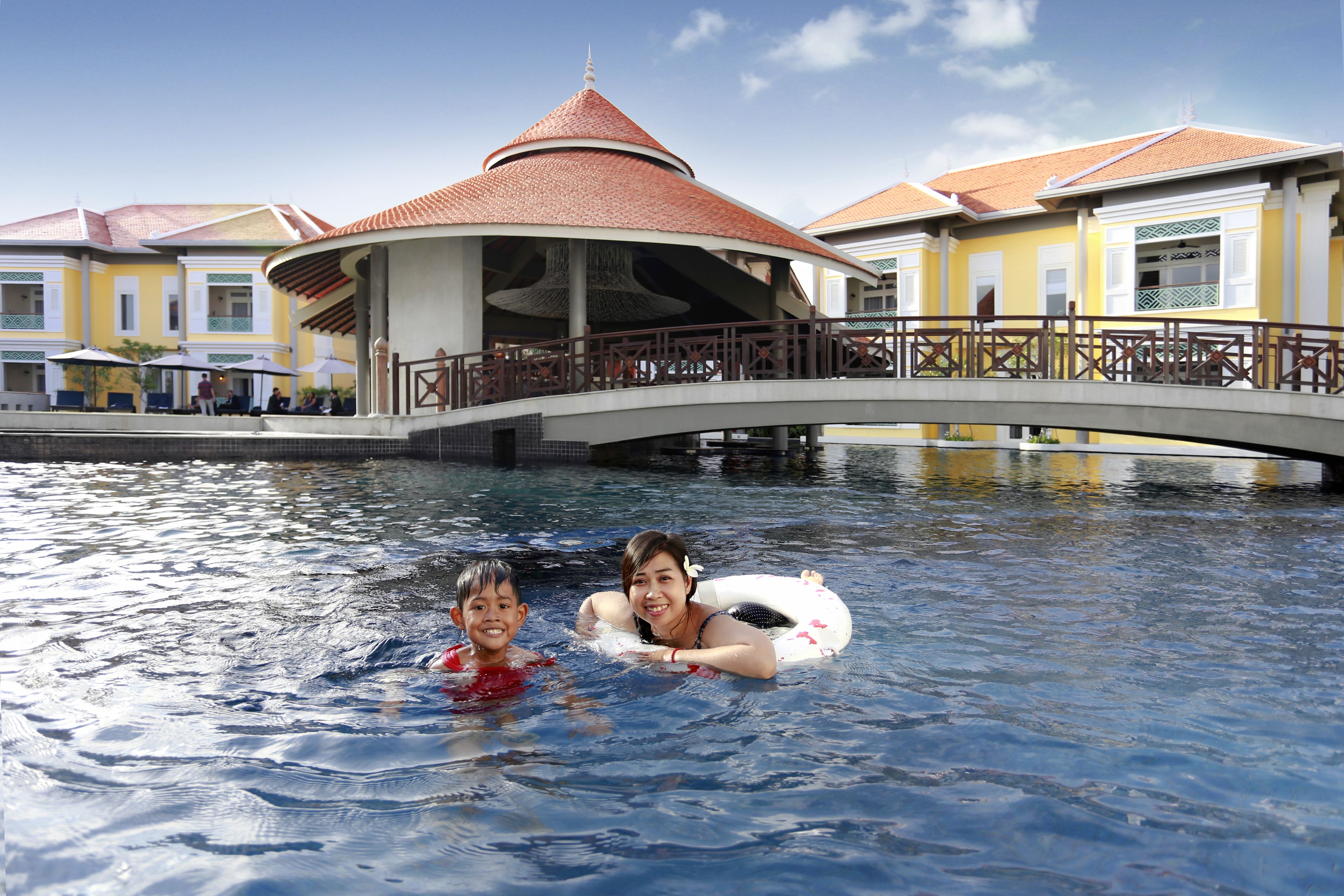Zona de piscina con un puente y edificios al fondo.