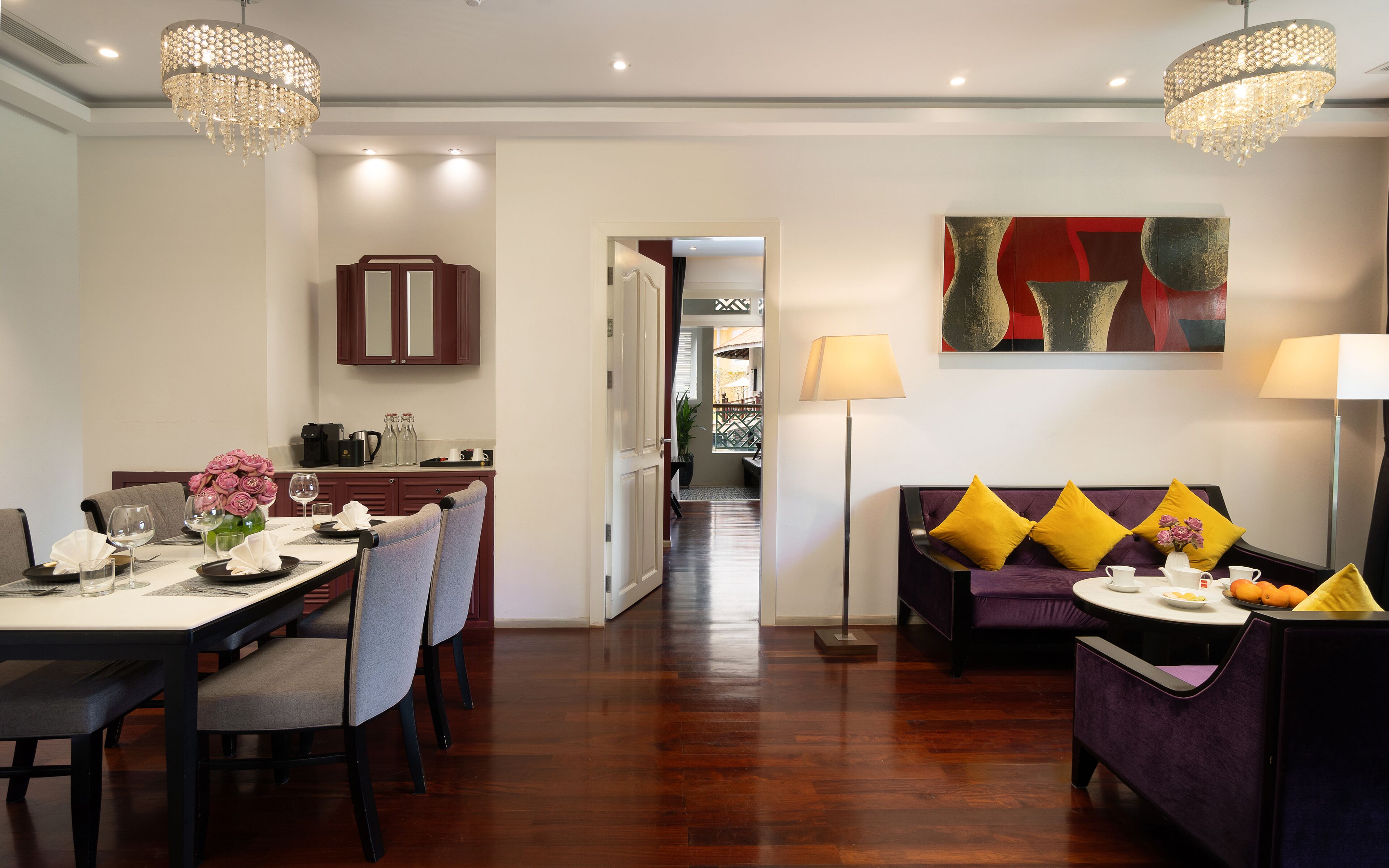 A dining area with a table set for two, a sofa with cushions, and a chandelier.