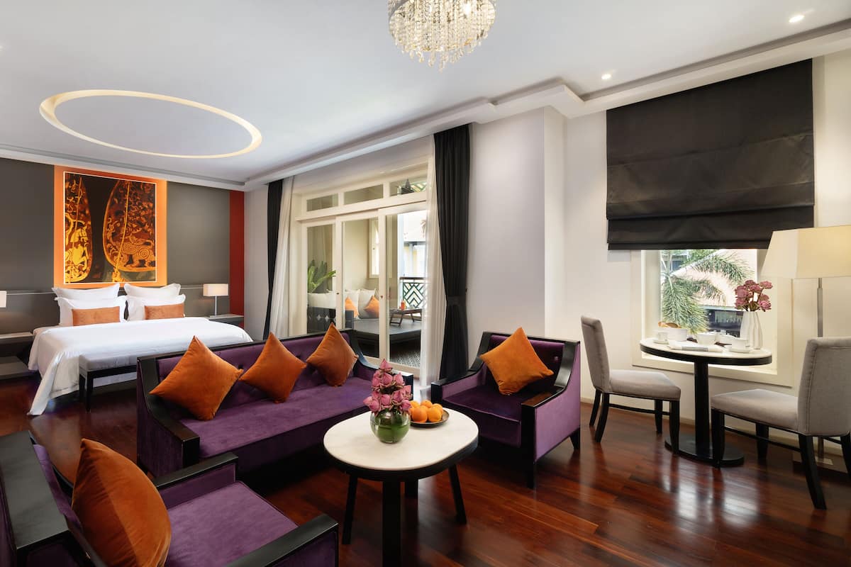 Ein Hotelzimmer mit einem Bett, einem violetten Sofa und einer Essecke mit Tisch und Stühlen.