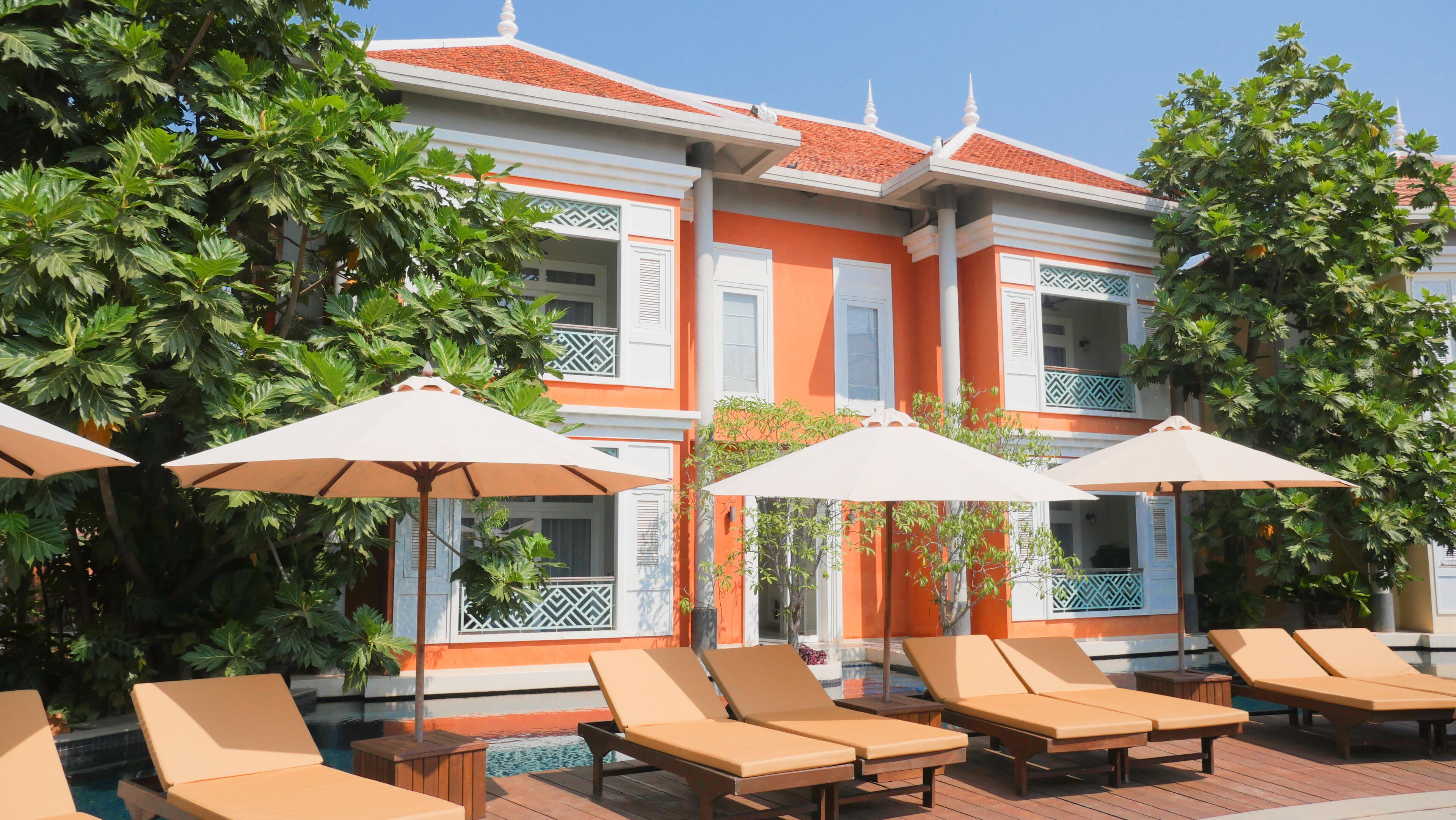 Um hotel com área de piscina, com espreguiçadeiras e guarda-sóis, rodeado por vegetação exuberante.
