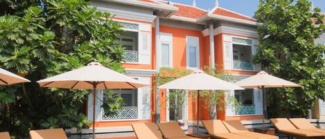 Um hotel com área de piscina, com espreguiçadeiras e guarda-sóis, rodeado por vegetação exuberante.