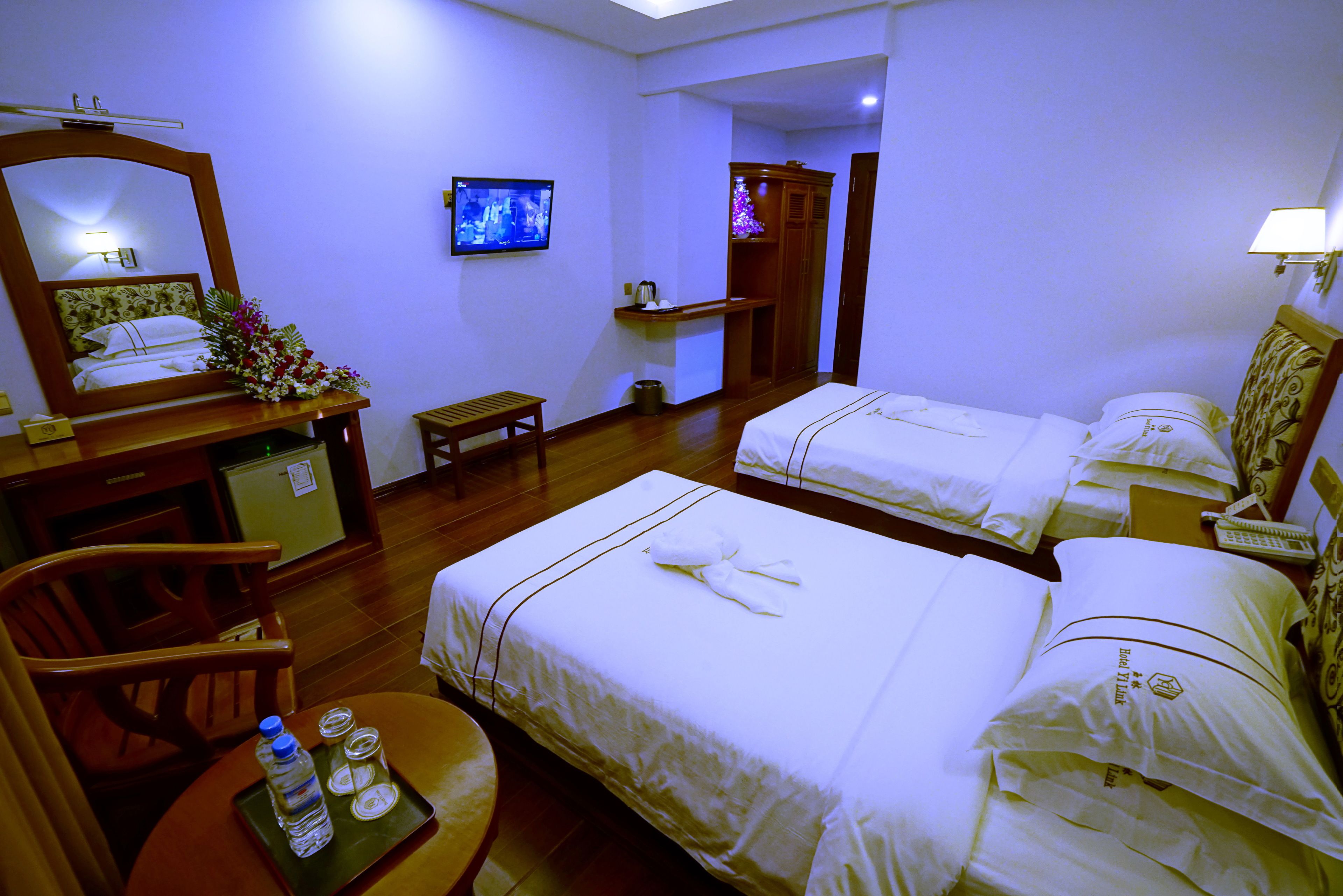 Habitación de hotel con dos camas, un escritorio con silla, una mesita con botellas de agua, televisión y espejo.