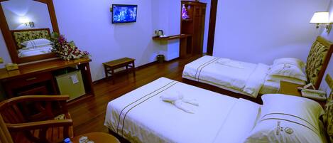 A hotel room with two beds, a desk with a chair, a small table with water bottles, a television, and a mirror.