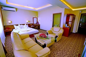 Habitación de hotel con cama, dos sillones, una mesita de centro con flores, cómoda y espejo.