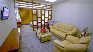 Una sala de estar con sofá, una mesa de centro con flores, televisor y un separador con cortinas.