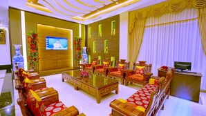 Un salón amplio con una gran mesa de centro de madera, varios sofás con cojines rojos y dorados, un televisor y una pared decorativa con espejos.