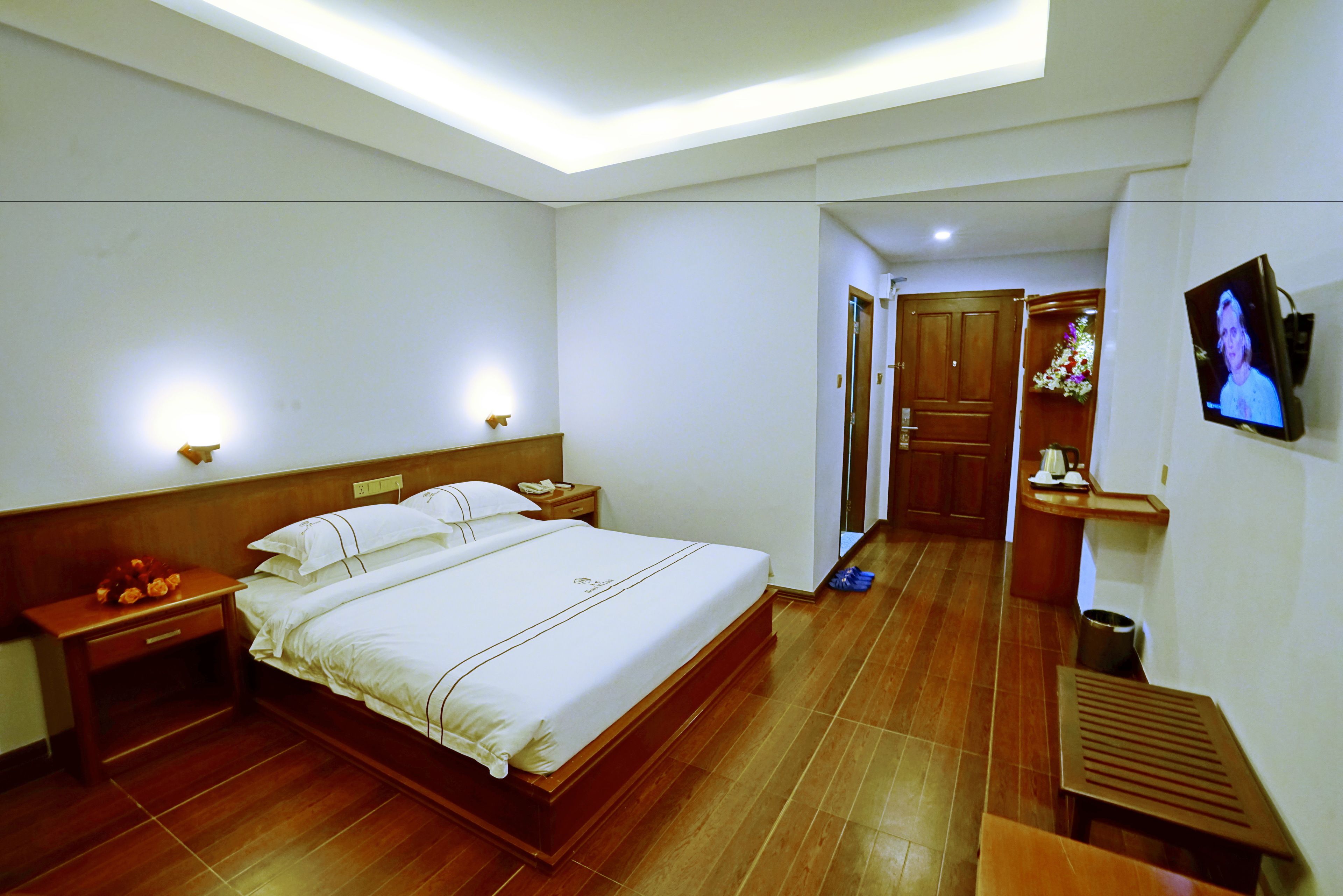 A hotel room with a large bed, bedside tables, a TV, and a wooden floor.