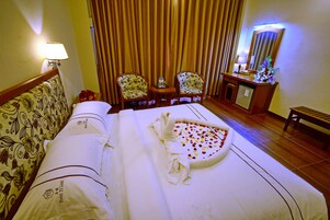 Una habitación de hotel con una cama, dos sillas, una mesita, un espejo y un banco.