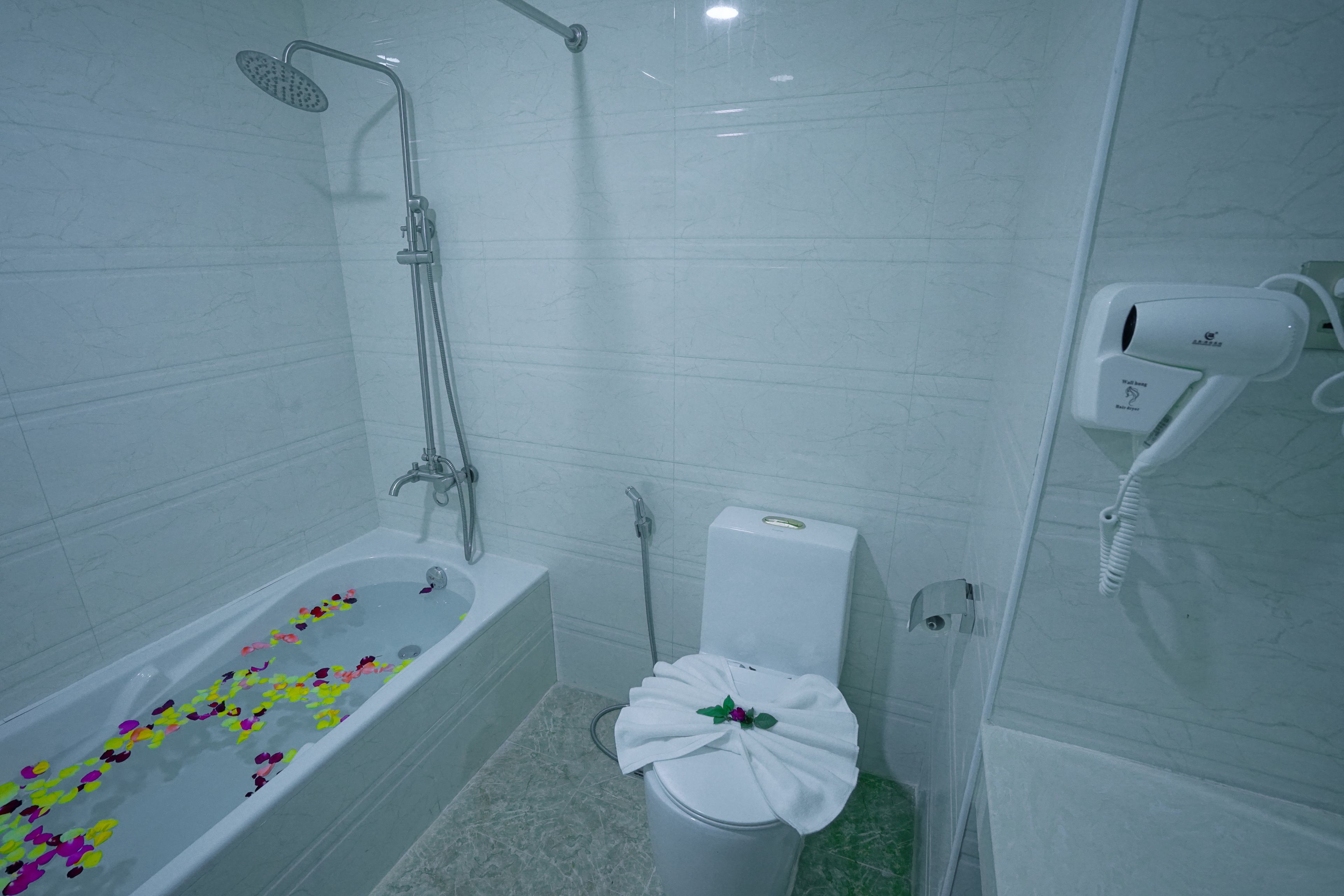 A bathroom with a bathtub, shower, toilet, and a hand dryer.
