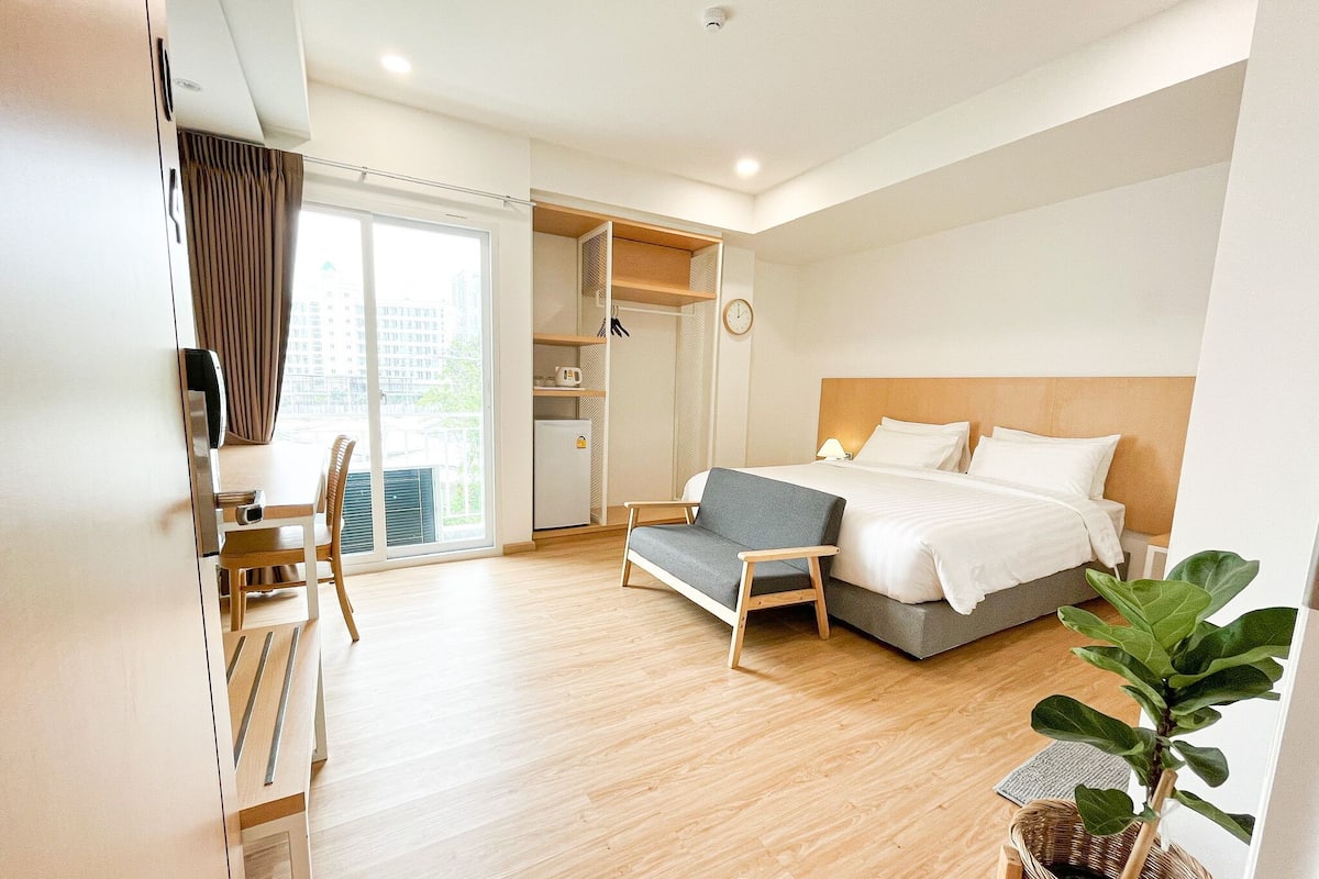 A modern hotel room with a bed, a sofa, a desk, and a large window.
