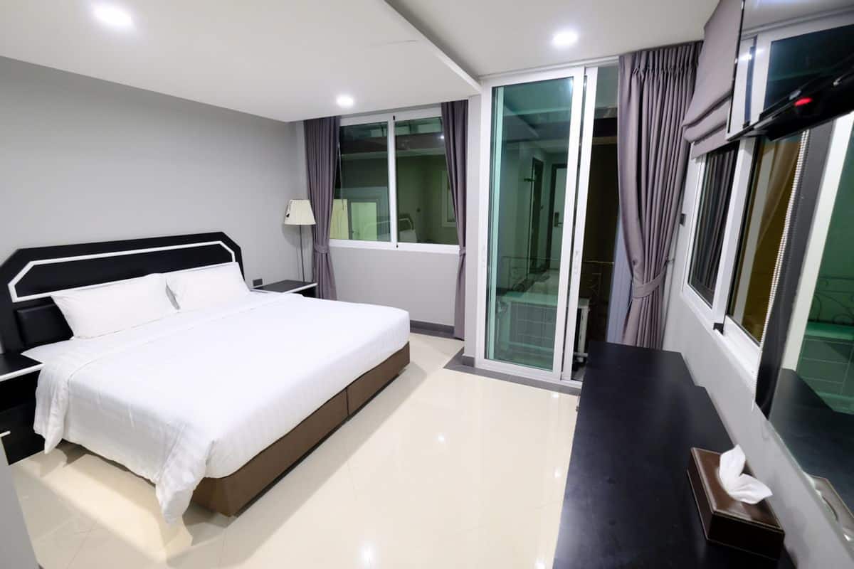 A modern hotel room with a large bed, a bedside table, a desk, and a sliding glass door to the balcony.
