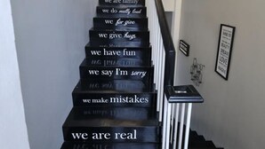 Una escalera con peldaños negros y barandillas blancas, cada peldaño grabado con una frase distinta sobre valores familiares.