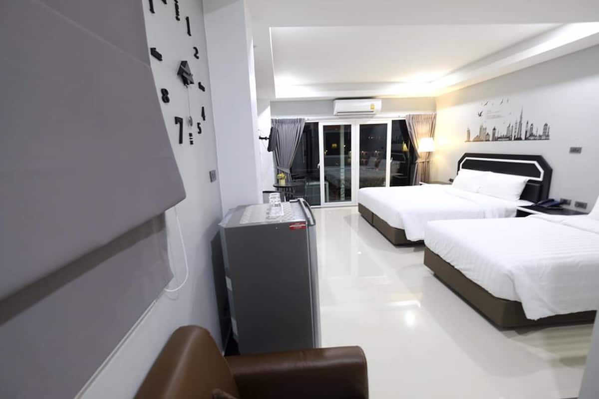 A hotel room with two beds, a desk, a refrigerator, and a view of the cityscape through the window.