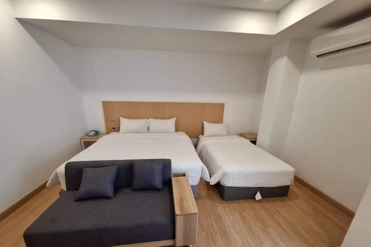 A hotel room with two single beds, a sofa, and a nightstand with a lamp.