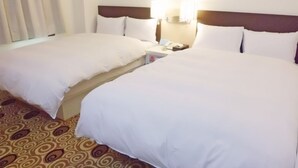 A hotel room with two beds, a nightstand with a phone, and a patterned carpet. - Foung Kou Hotel (Magong)