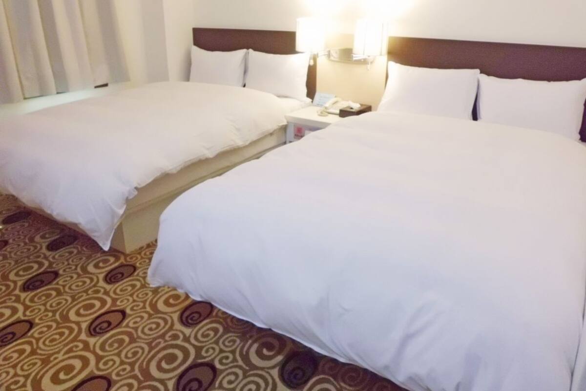 A hotel room with two beds, a nightstand with a phone, and a patterned carpet.