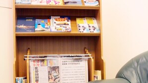 A bookshelf with books and magazines, a leather couch, and a table with a decorative item. - Foung Kou Hotel (Magong)