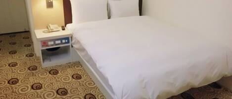 A hotel room with a bed, a nightstand with a lamp, and a patterned carpet.